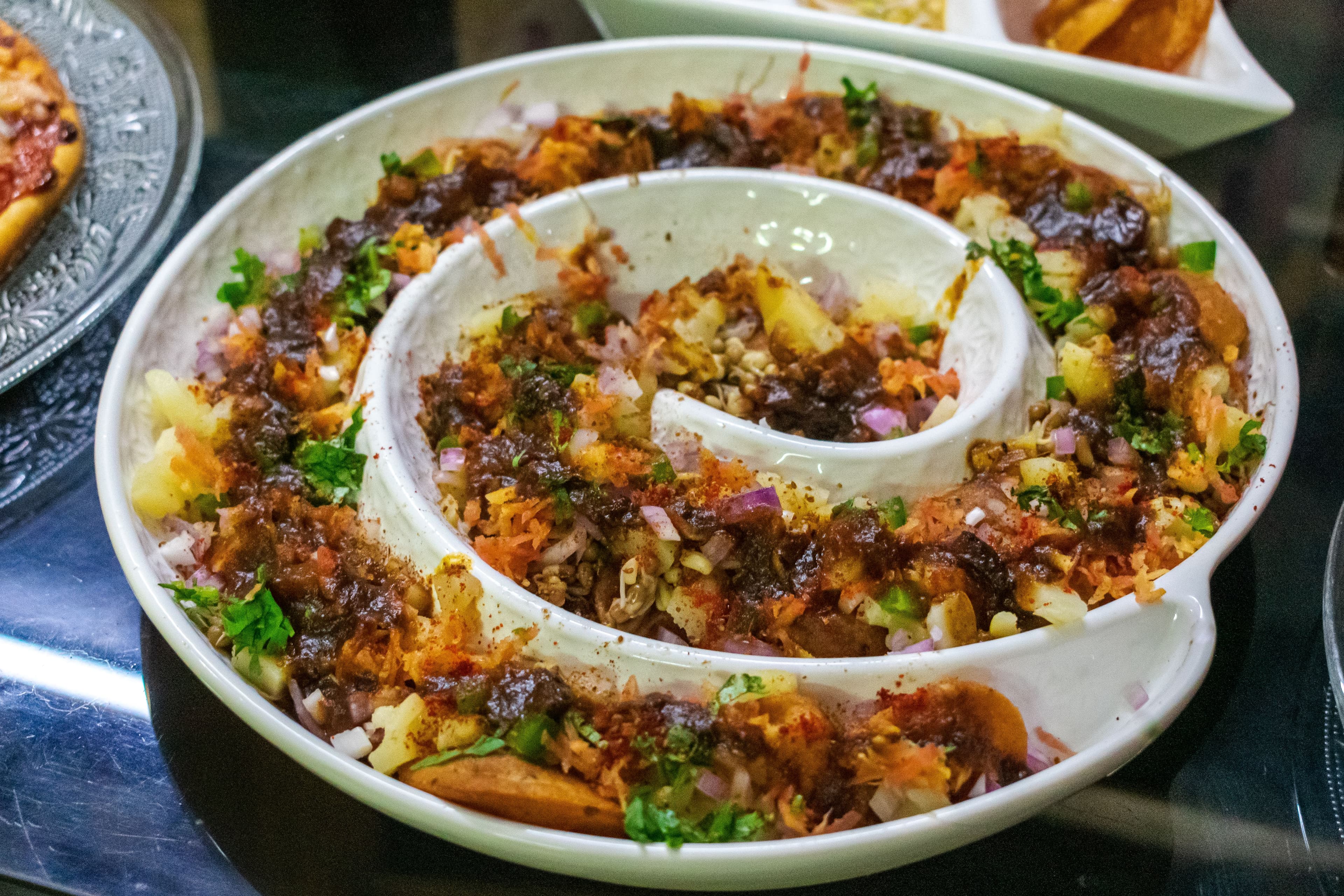Spiral platter of chaat beside a slice of pizza at a wedding buffet