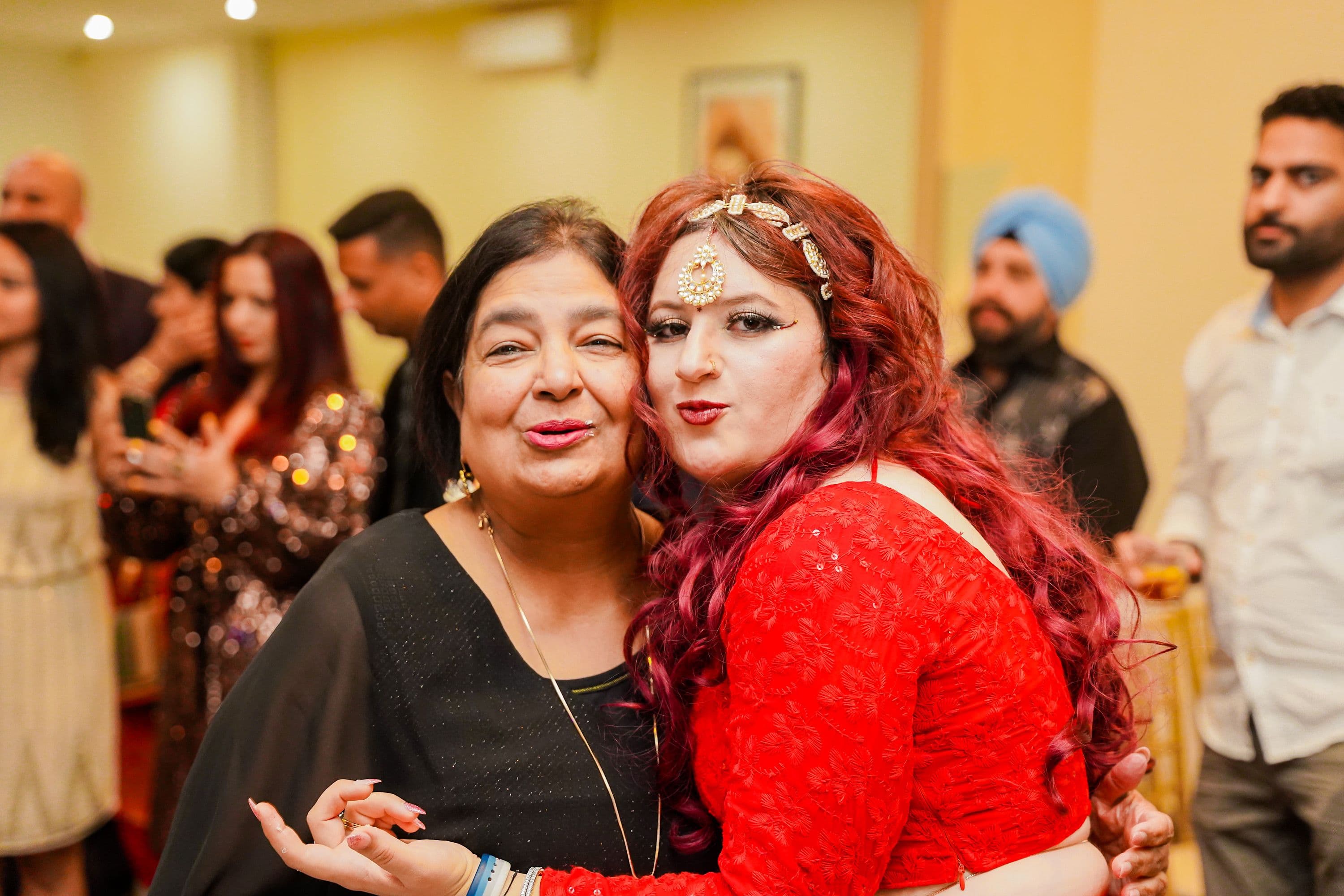 Two women in traditional attire posing cheek to cheek at a reception