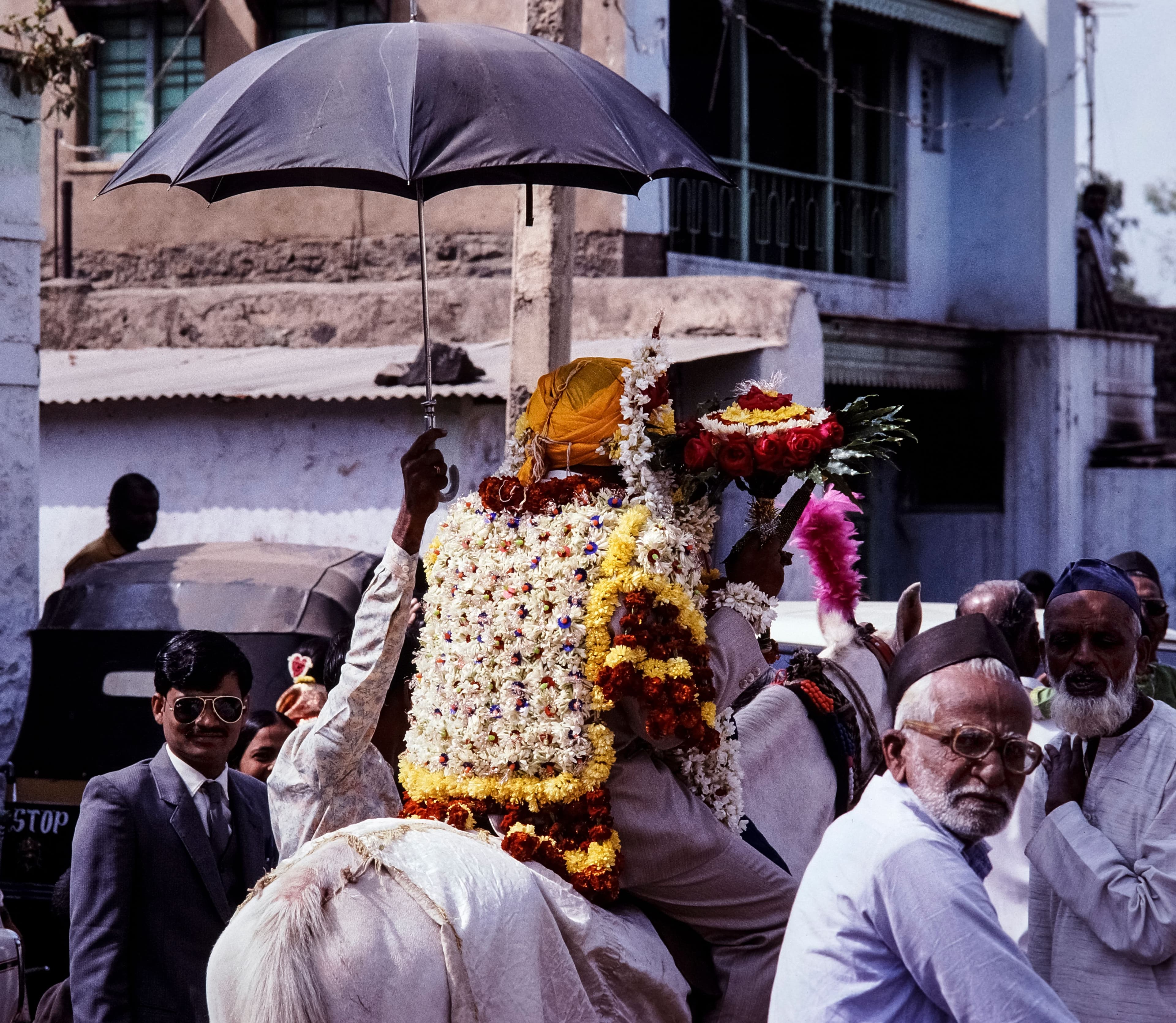 A groom fully veiled in a flower sehra on horseback under a black umbrella